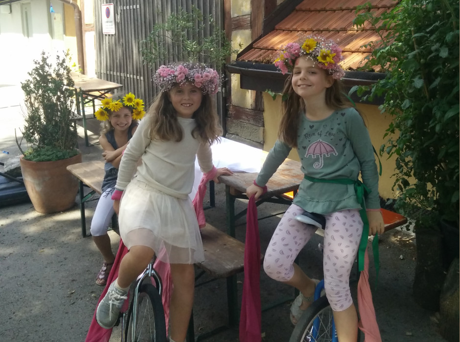 Drei Mädchen mit Blumenkränzen auf Einrädern